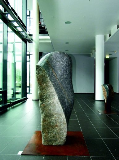 Vom Künstler Jan Moritz Stahl - Steinerne Skulptur in modernem Raum mit glatten Wänden und Fliesenboden.