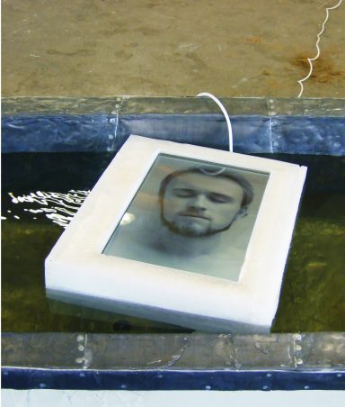 Künstler Jan Moritz Stahl - Ein Rahmen mit einem abgedruckten Gesicht schwimmt auf Wasser.