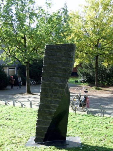 Künstler Jan Moritz Stahl - Schwarze Steinskulptur in einem Park, umgeben von Bäumen und grüner Wiese.