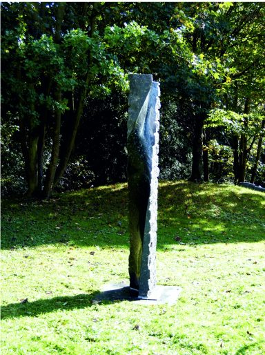Künstler Jan Moritz Stahl - Schmale, vertikale Skulptur aus schwarzem Material in einem grünen Park.