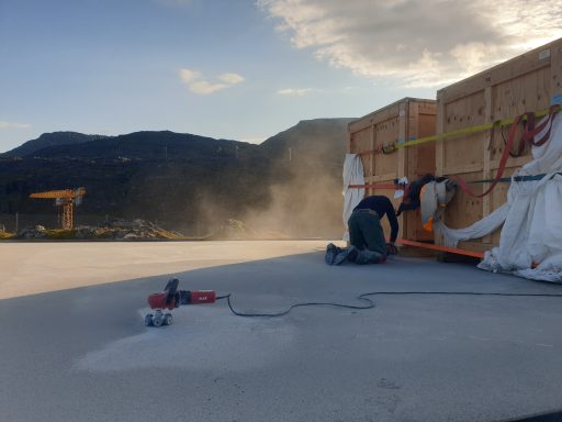 Arbeiter verpackt Material auf dem Dach, Staubwirbel im Hintergrund, Berglandschaft.