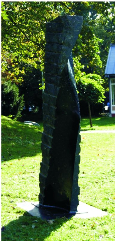 Künstler Jan Moritz Stahl - Schmale, hohe Skulptur aus schwarzem Material, umgeben von grünem Gras und Bäumen.