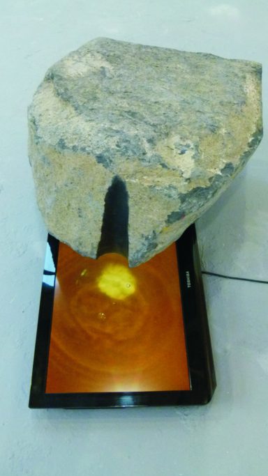 Künstler Jan Moritz Stahl - Ein großer Stein steht über einem flachen, orangefarbenen Bildschirm mit gelber Leuchte.