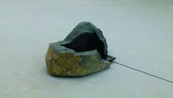 Künstler Jan Moritz Stahl - Graue, natürliche Steinform mit einer Öffnung in der Mitte, auf einem hellen Boden.